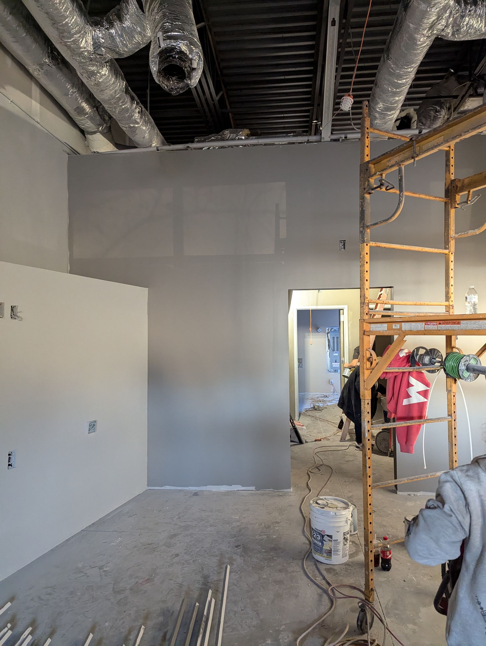 Interior of a commercial space under construction with grey painted walls, exposed ceiling ductwork, and yellow scaffolding.
