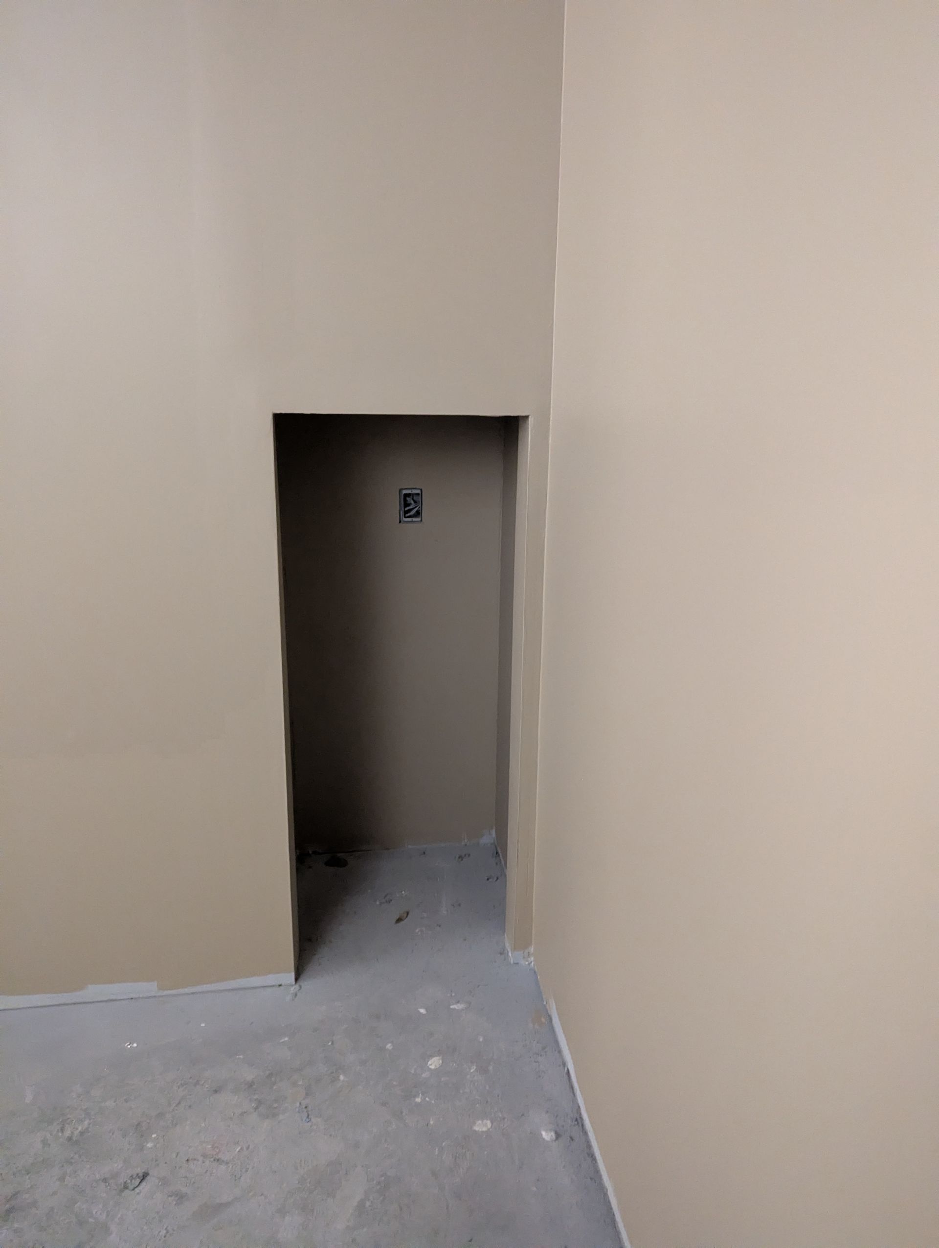 A beige room with an empty, rectangular wall cutout leading to a dark alcove containing an electrical outlet.