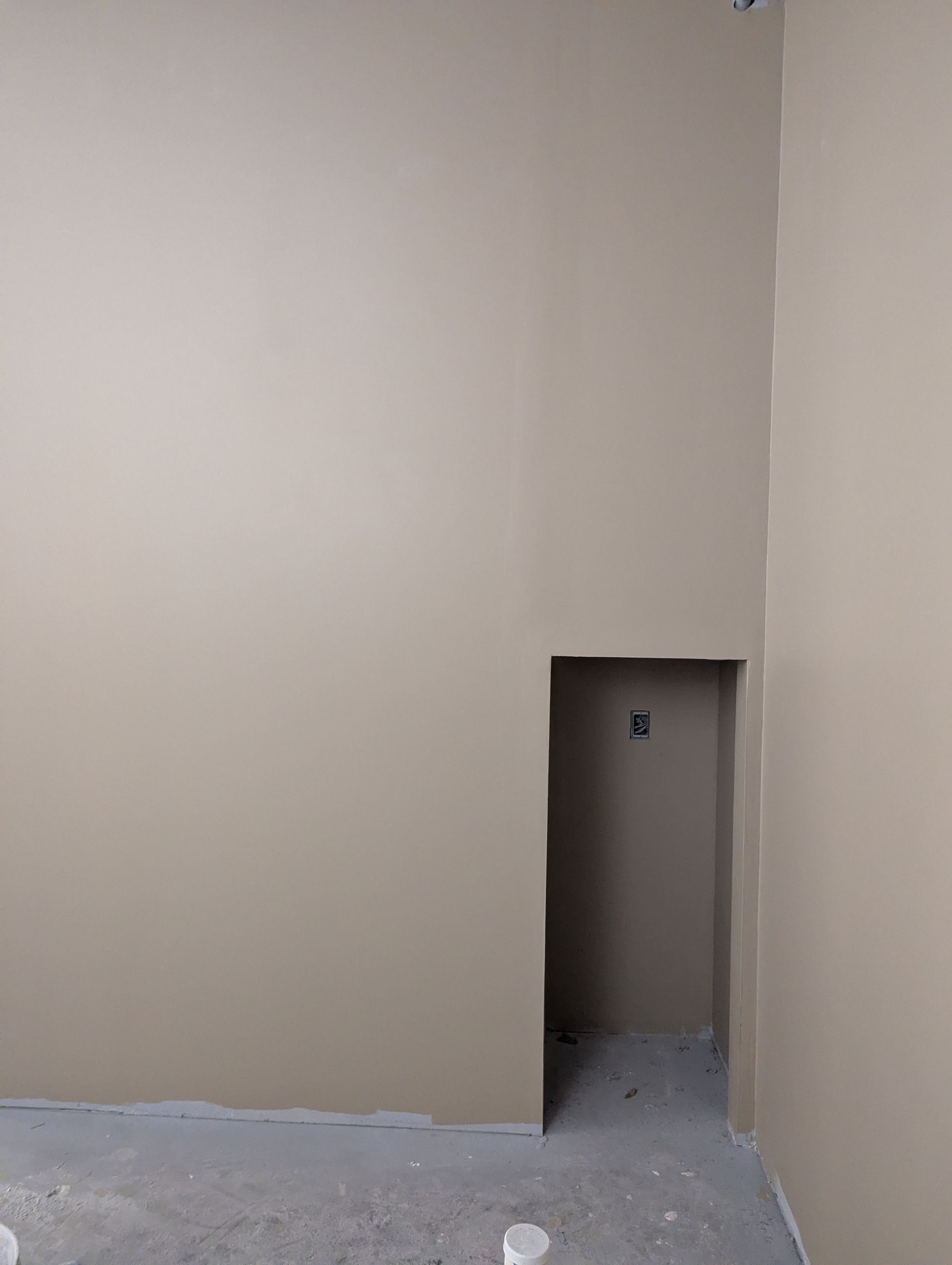 A beige wall with a recessed rectangular opening and unfinished flooring at the bottom.