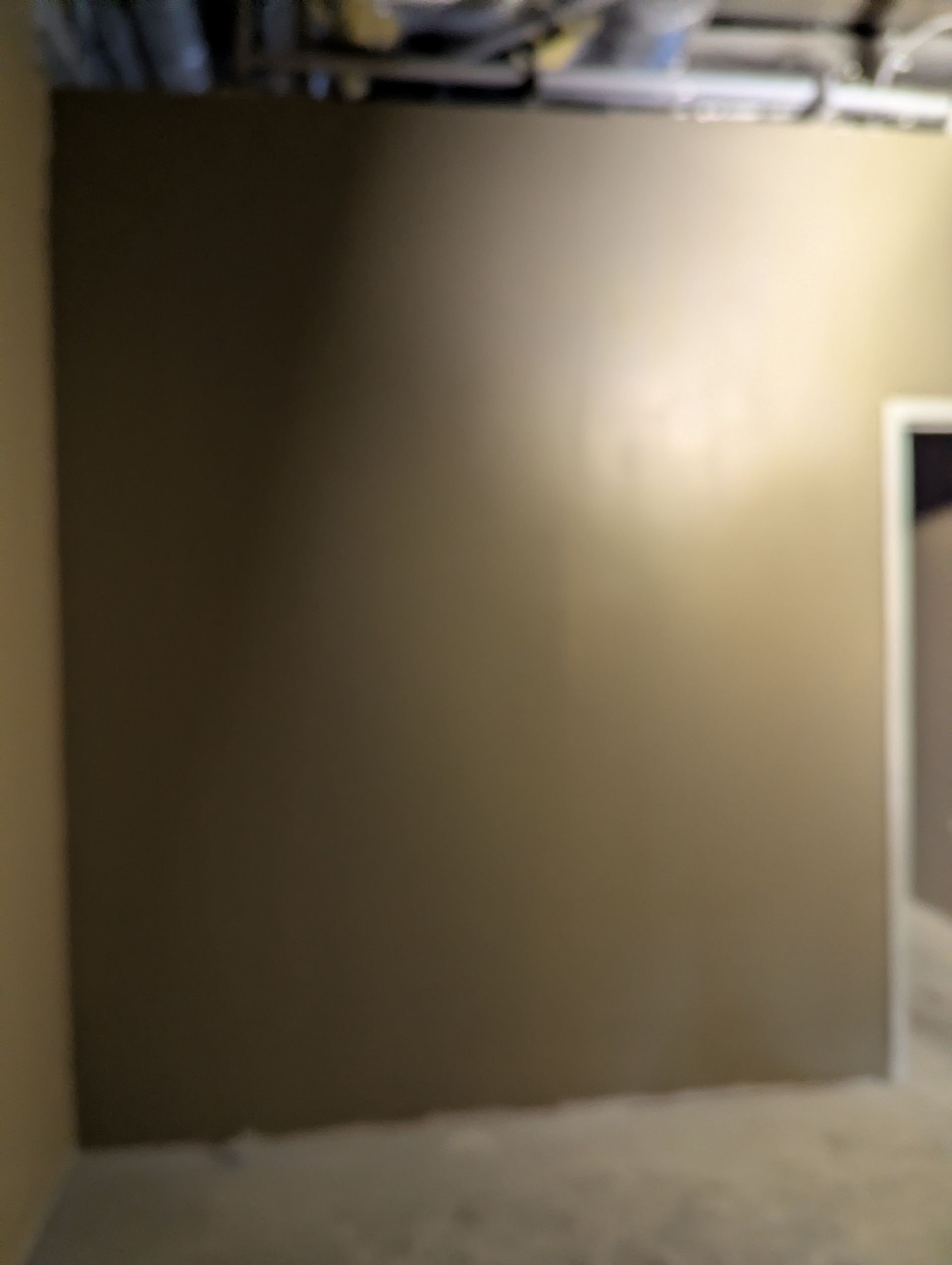A newly painted, smooth brown wall in a room under construction with exposed ceiling pipes and an unfinished floor.