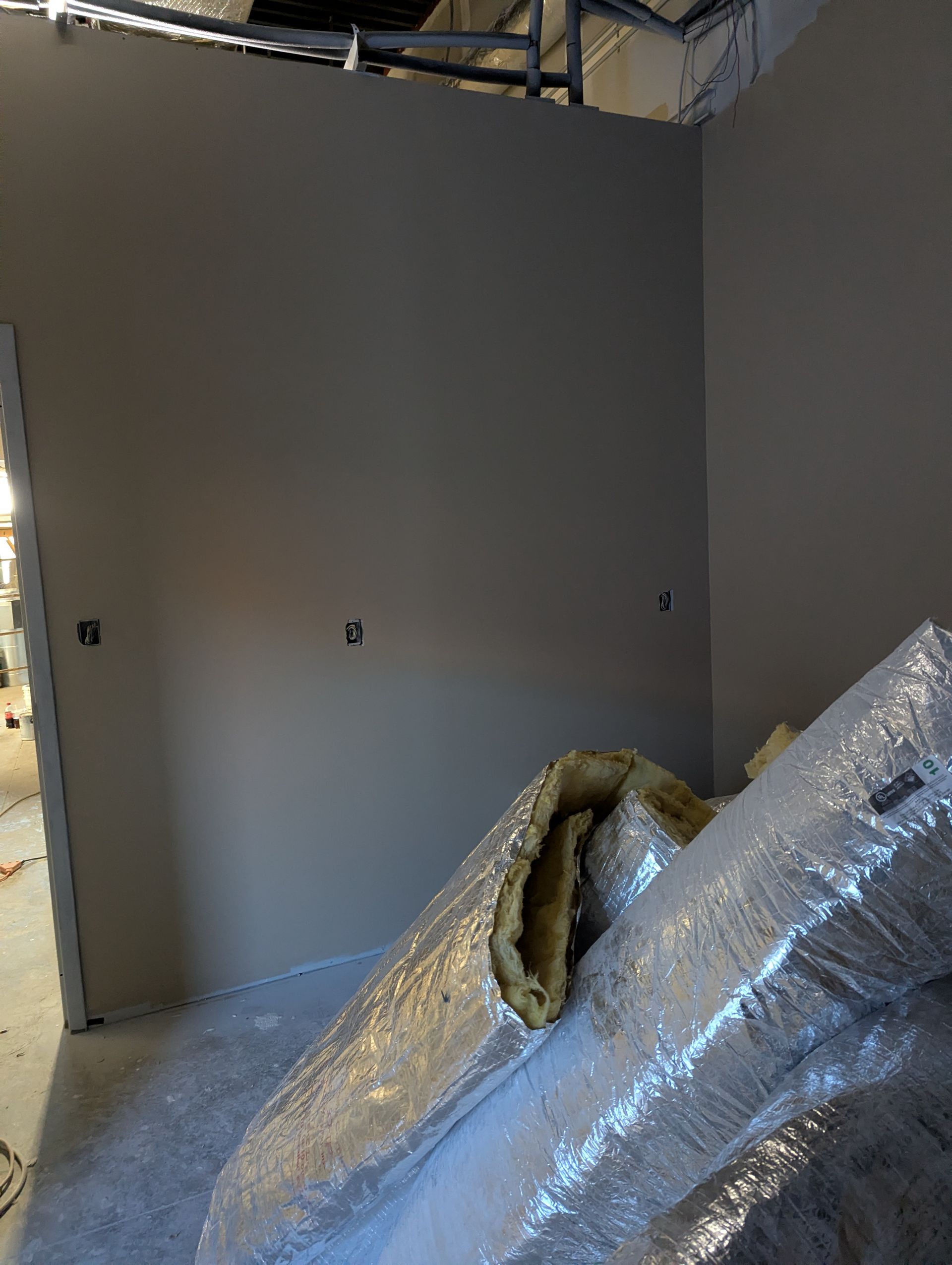 A gray interior wall under construction with exposed overhead ductwork and insulation materials in the foreground.