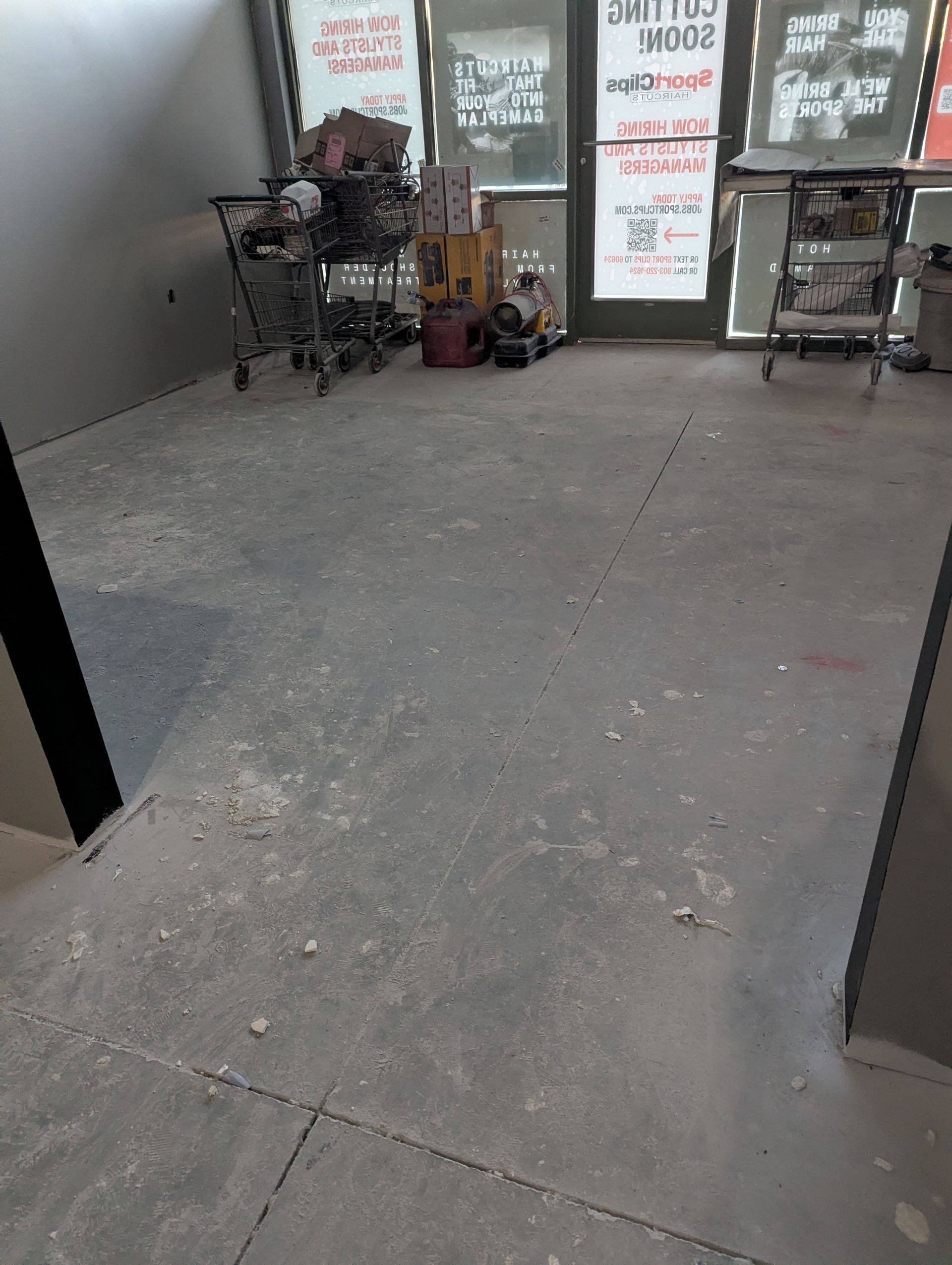 A view of a messy, unfinished floor leading to glass doors with signs, featuring two metal shopping carts.