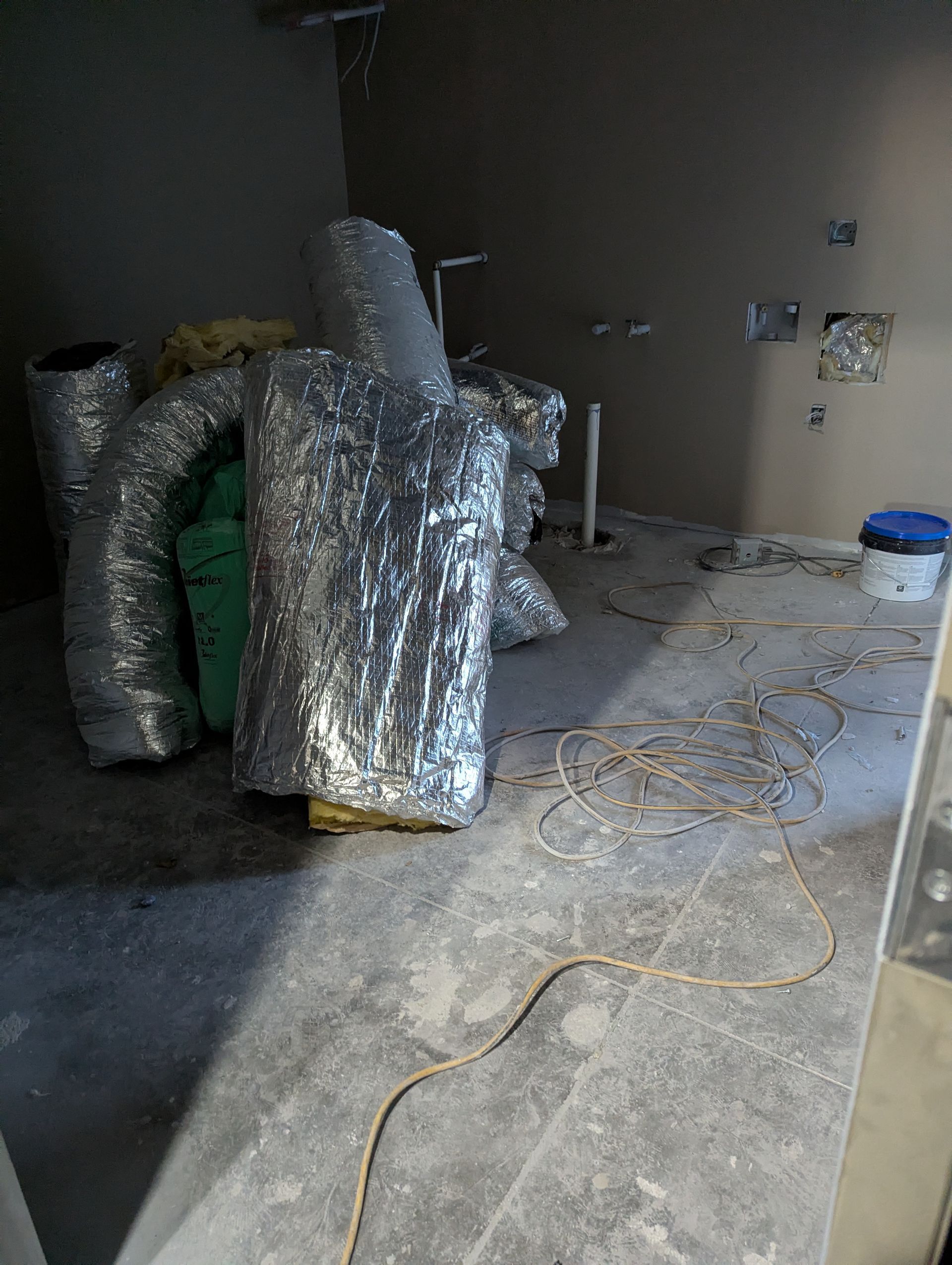 Unfinished room with exposed ductwork, loose wires, and a bucket on a concrete floor during construction.
