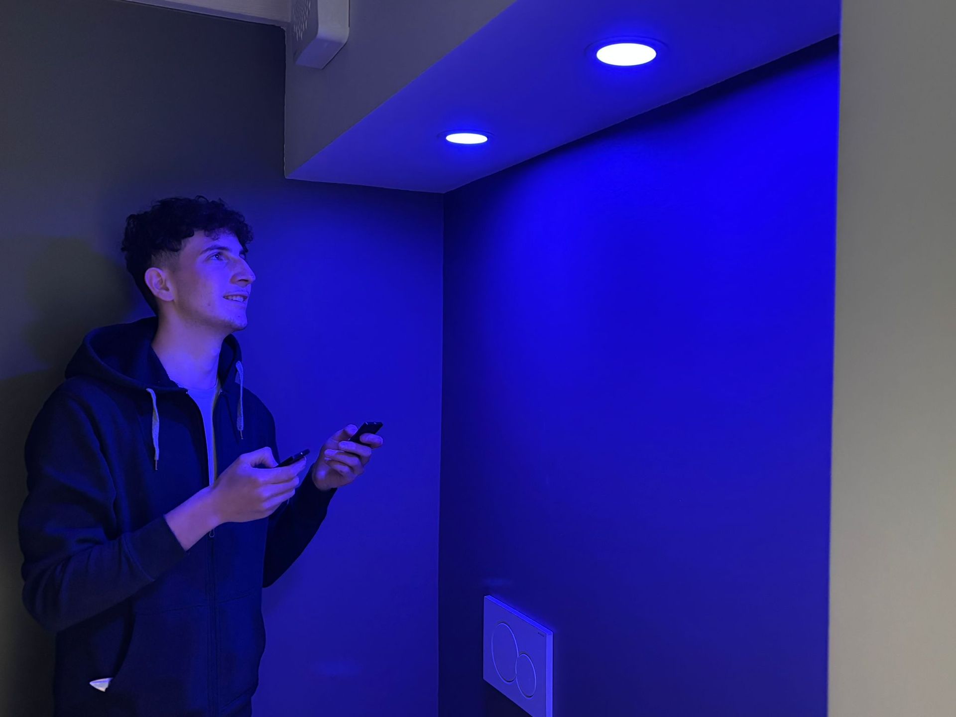 Un giovane tiene in mano un cellulare davanti a un muro blu.