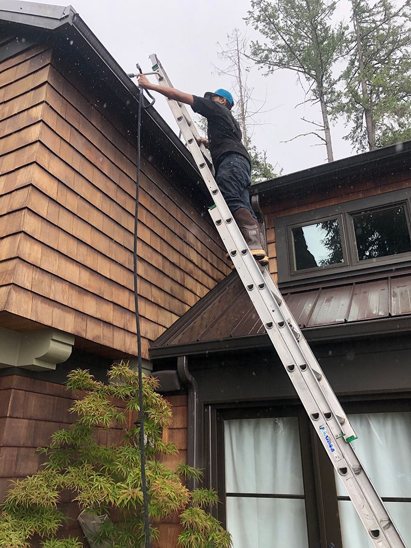 A man is standing on a ladder on the side of a house.