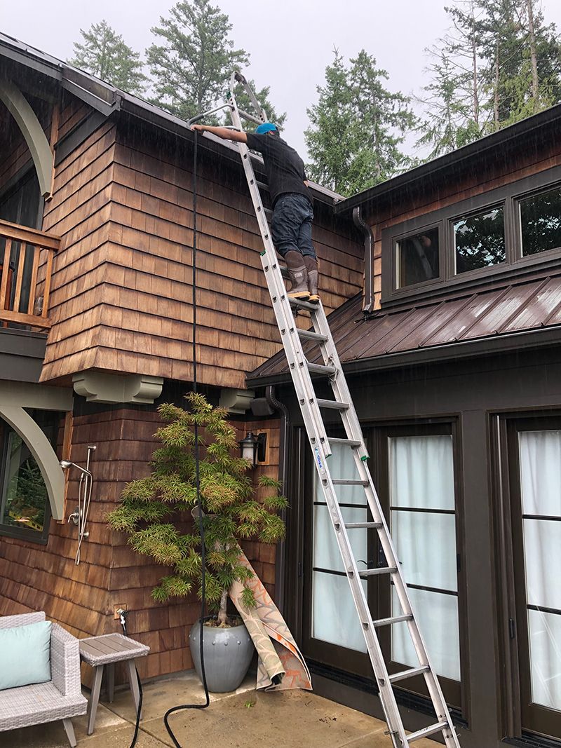 A man is standing on a ladder on the side of a house.