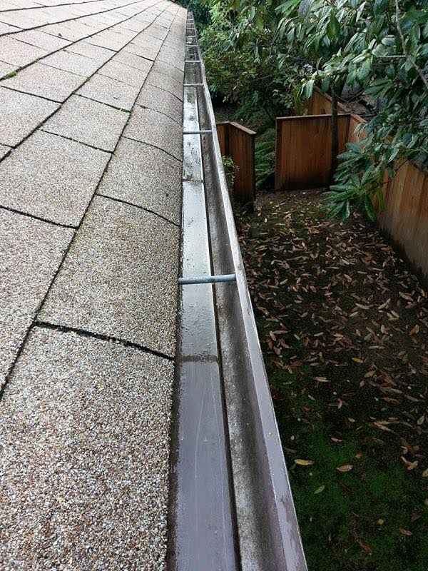 A gutter on the side of a roof next to a wooden fence.