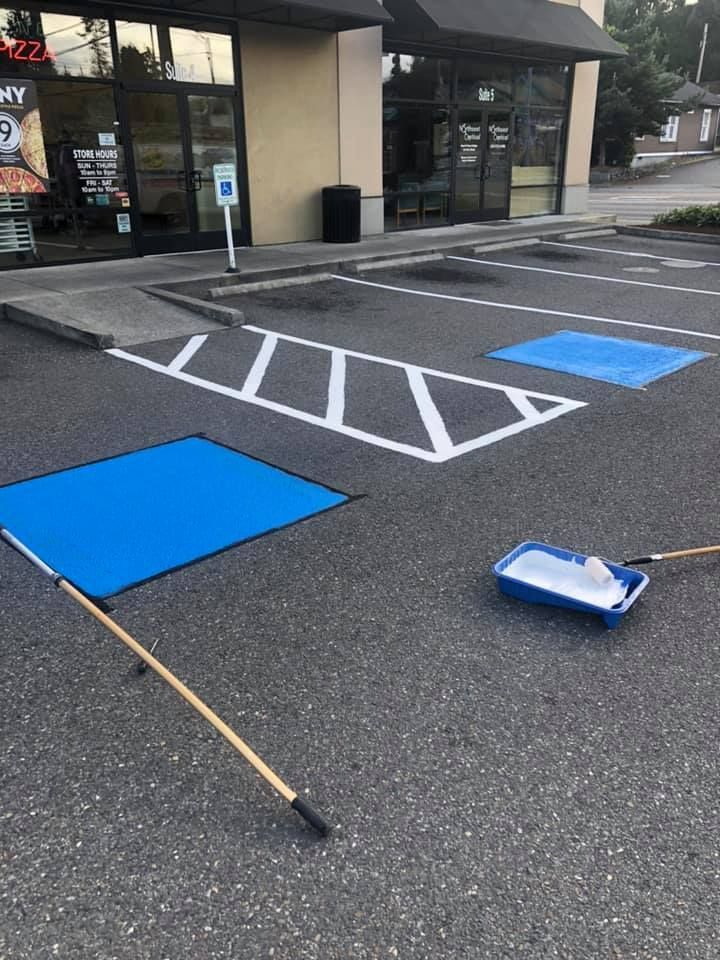 A parking lot is being painted blue in front of a store.