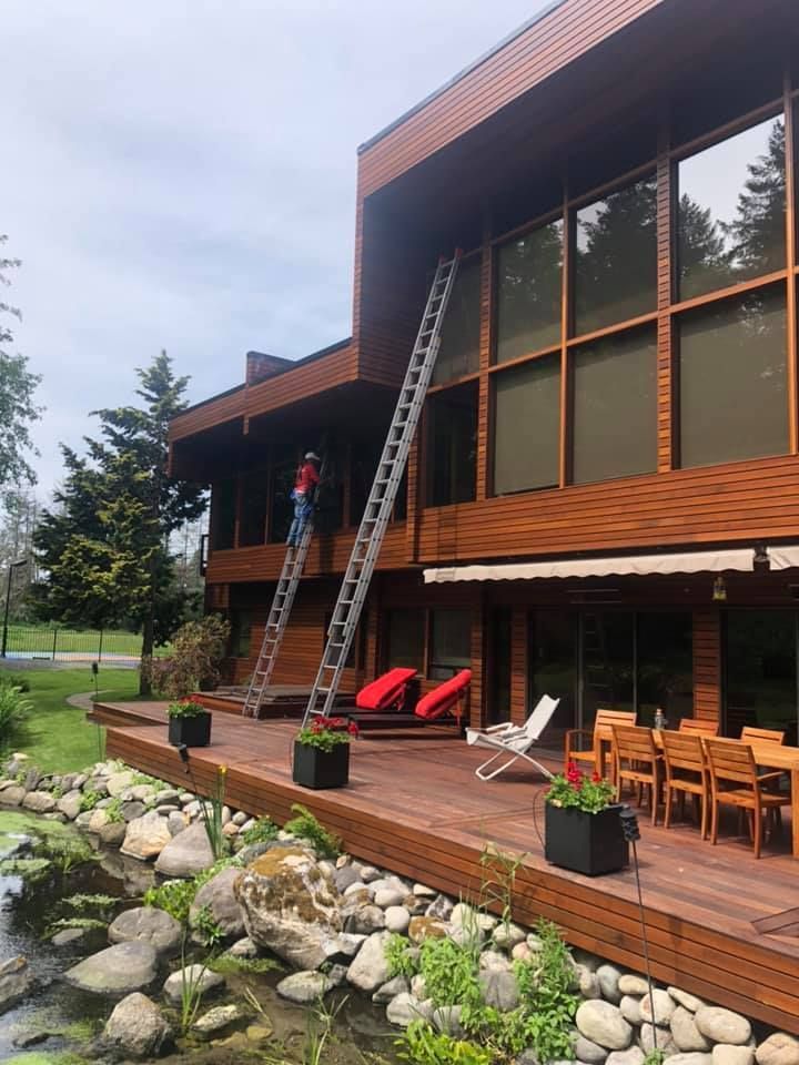 A man is standing on a ladder in front of a large wooden house.