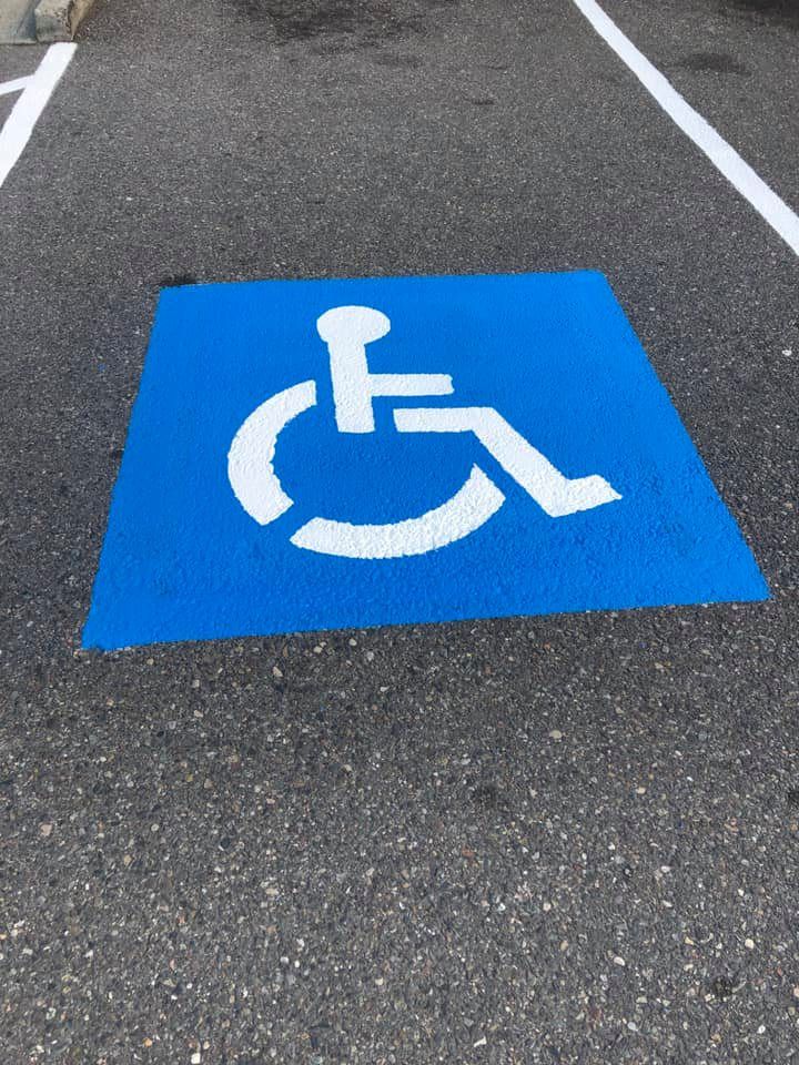 A blue handicap sign is painted on the ground in a parking lot