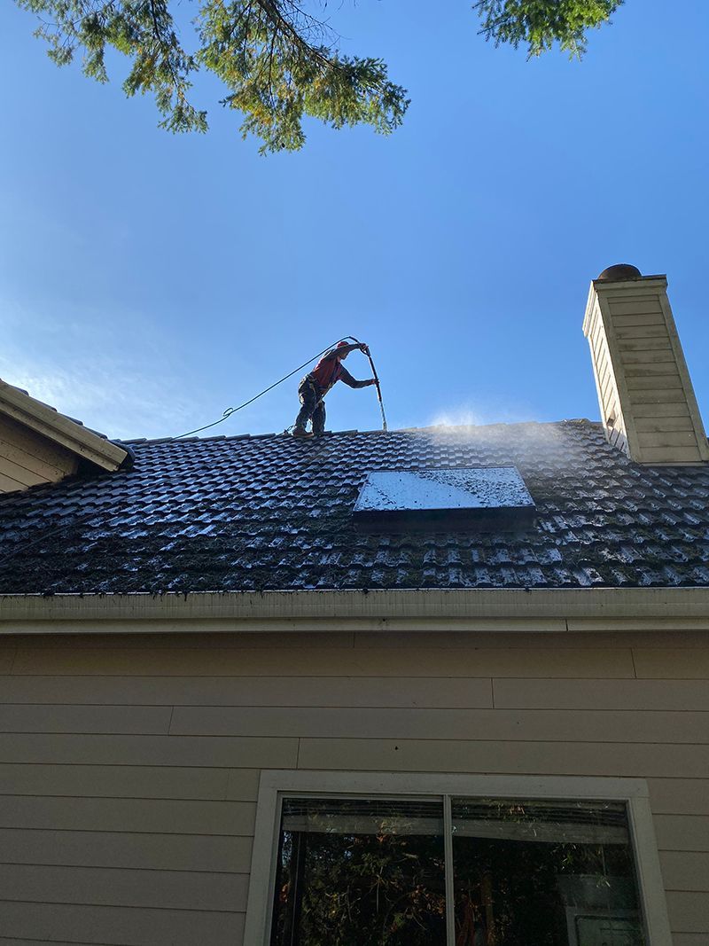 A man is cleaning the roof of a house with a pressure washer.