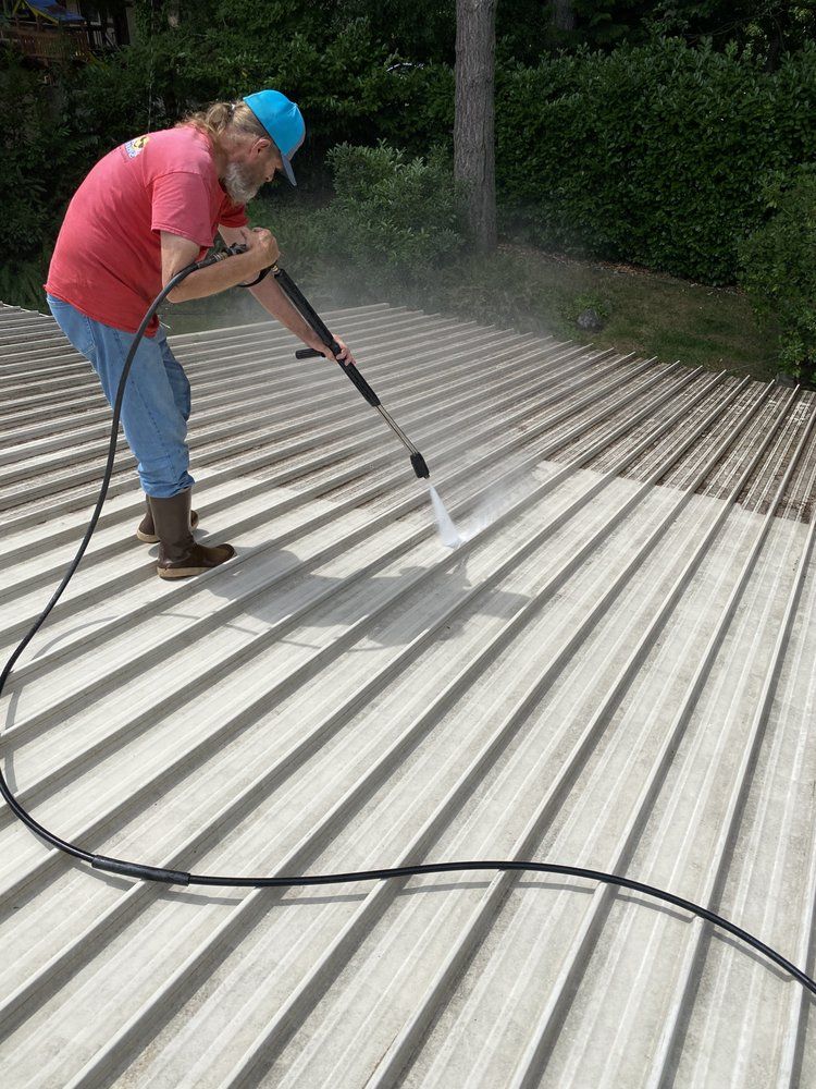A person is cleaning the roof of a house with a pressure washer.