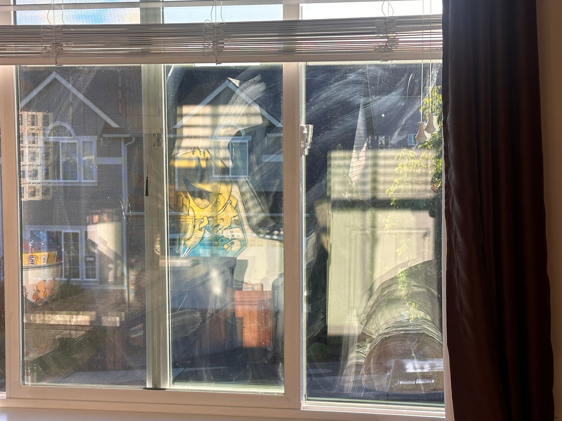 A window with blinds on it and a reflection of a house in the window.