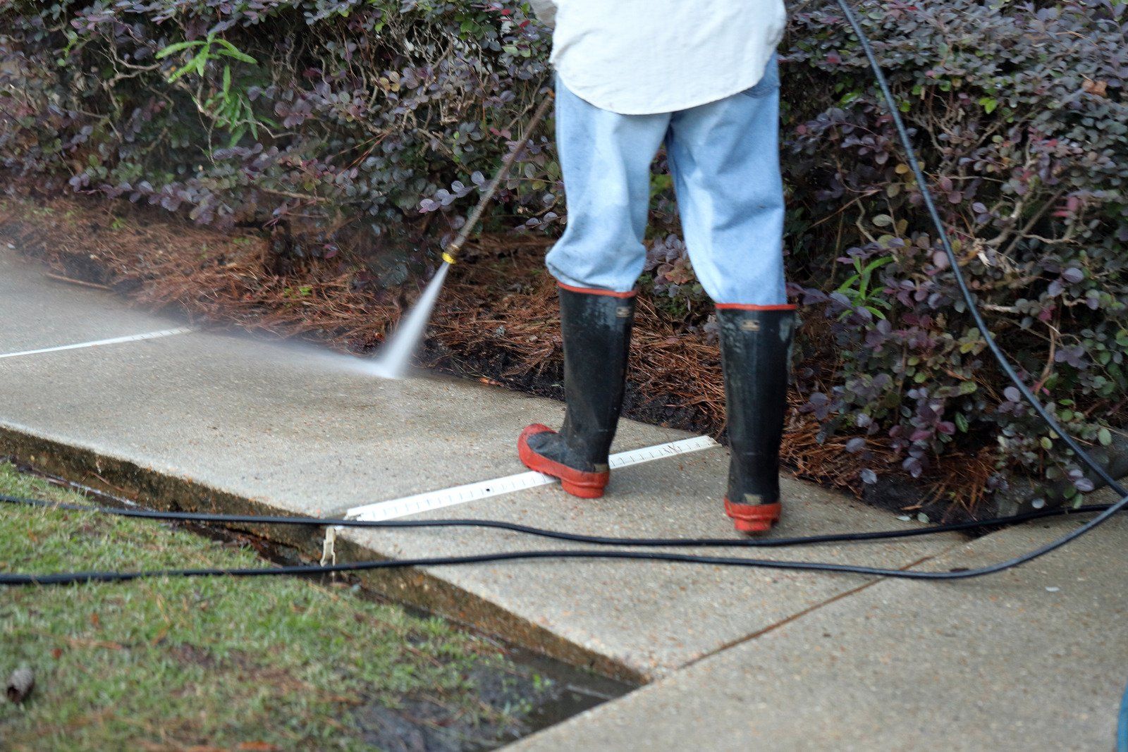 A person is using a high pressure washer to clean a sidewalk.