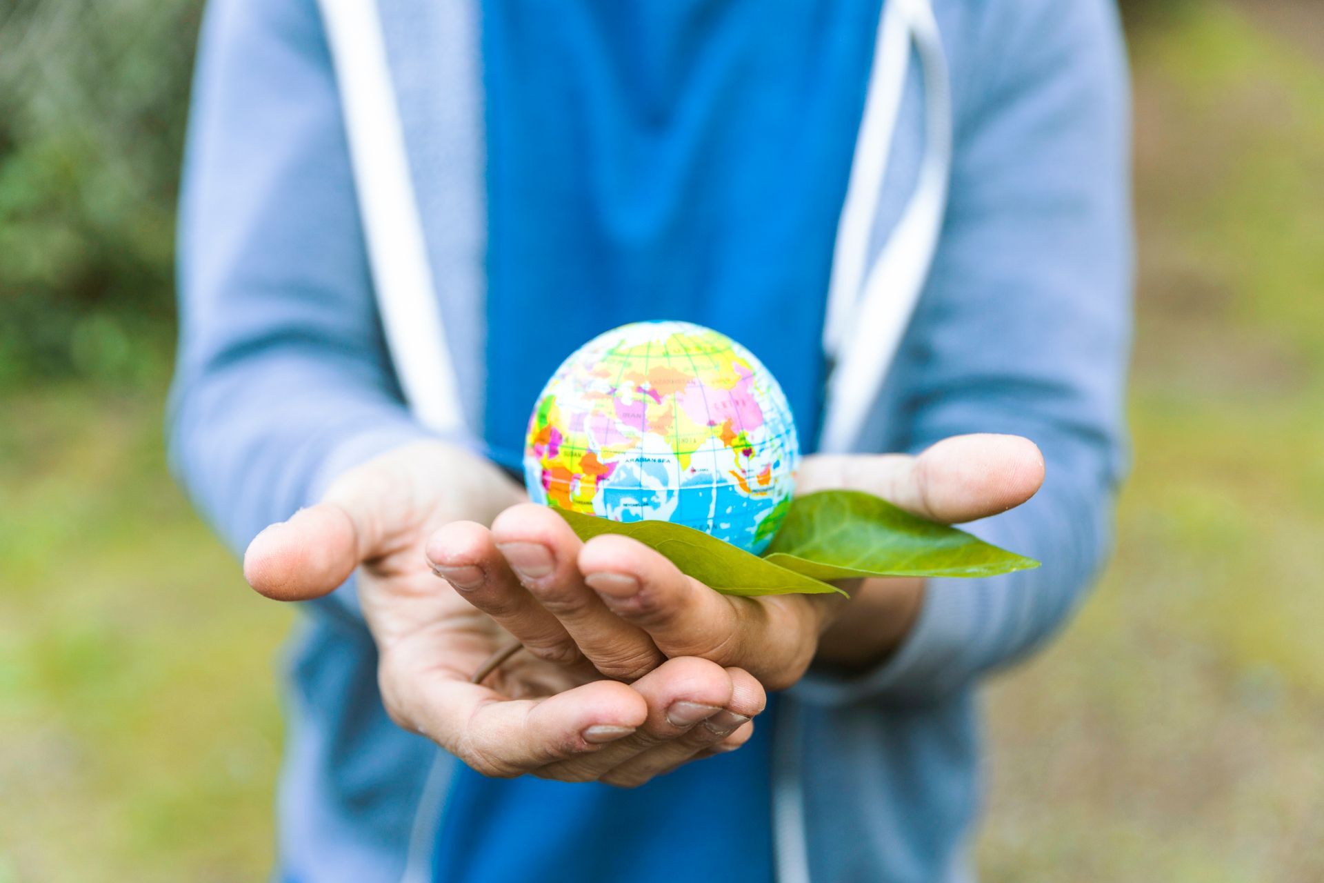 Una persona sostiene en sus manos un globo terráqueo con una hoja sobre él.