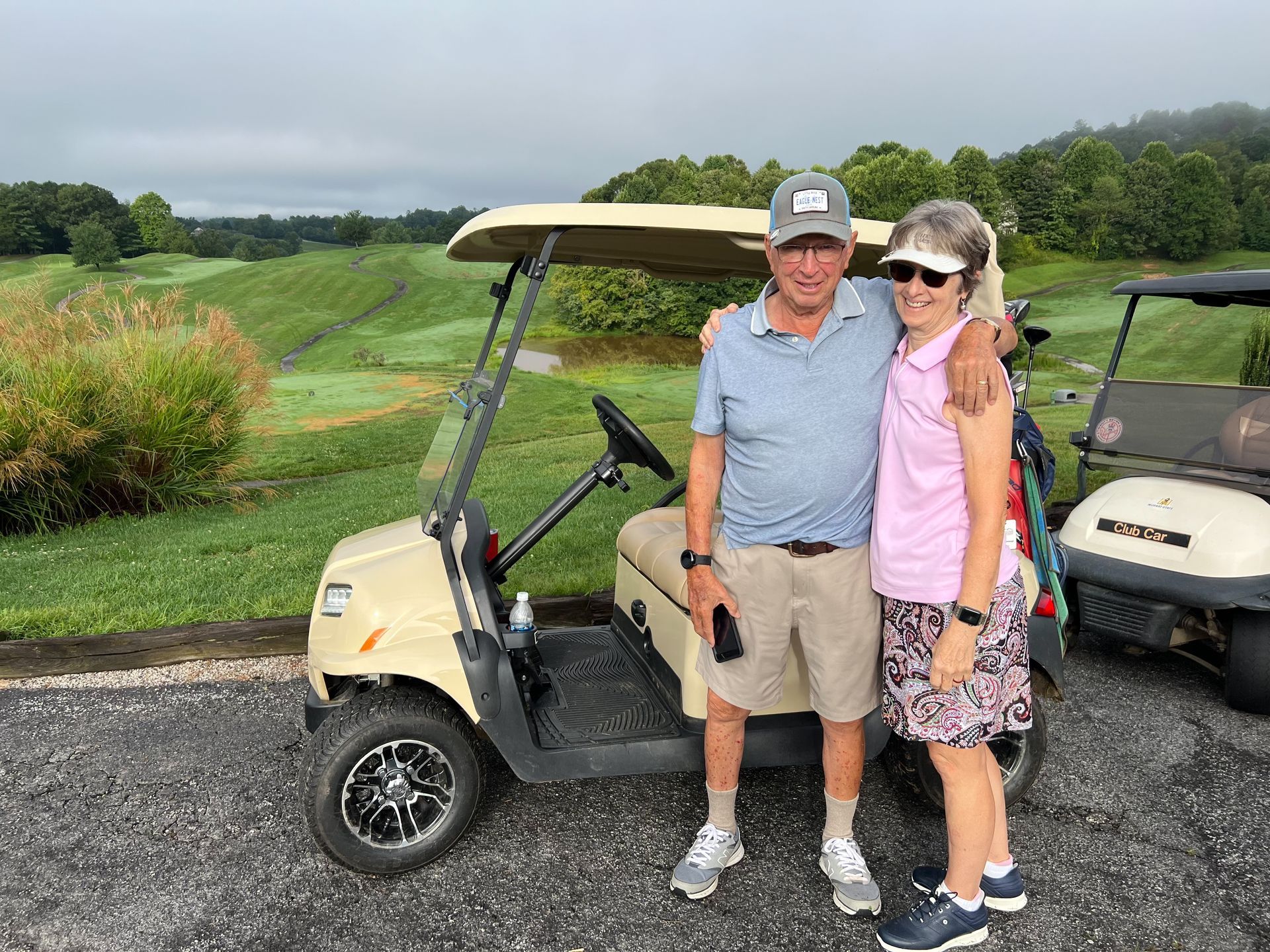 A man and a woman are standing next to a golf cart on a golf course.