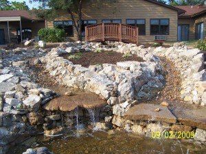 There is a waterfall in the middle of a rocky area in front of a house.