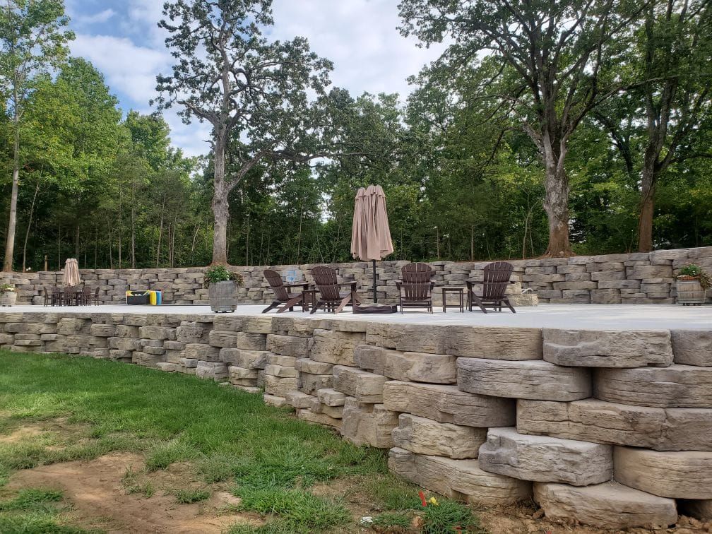 A large stone wall surrounds a patio with chairs and umbrellas.