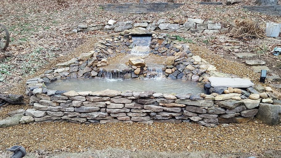 A small waterfall is surrounded by rocks and gravel in a garden.
