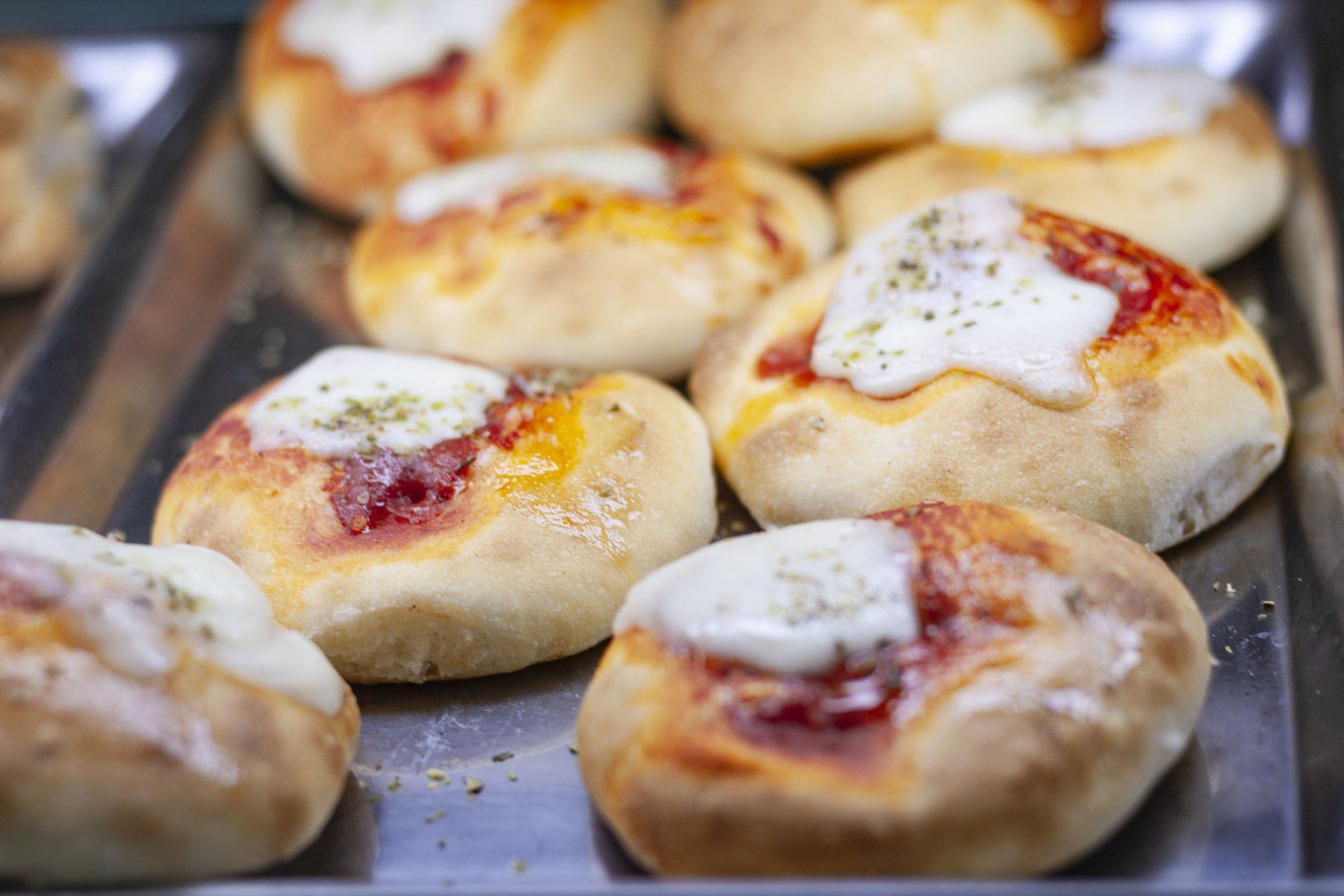 Primo piano di diverse piccole pizze cotte al forno con salsa di pomodoro e formaggio fuso su un vassoio di metallo.