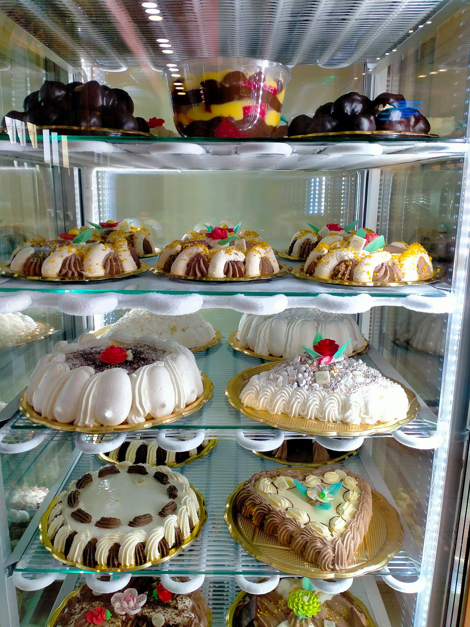 Vetrina piena di torte e dessert colorati, ambientata in una panetteria.