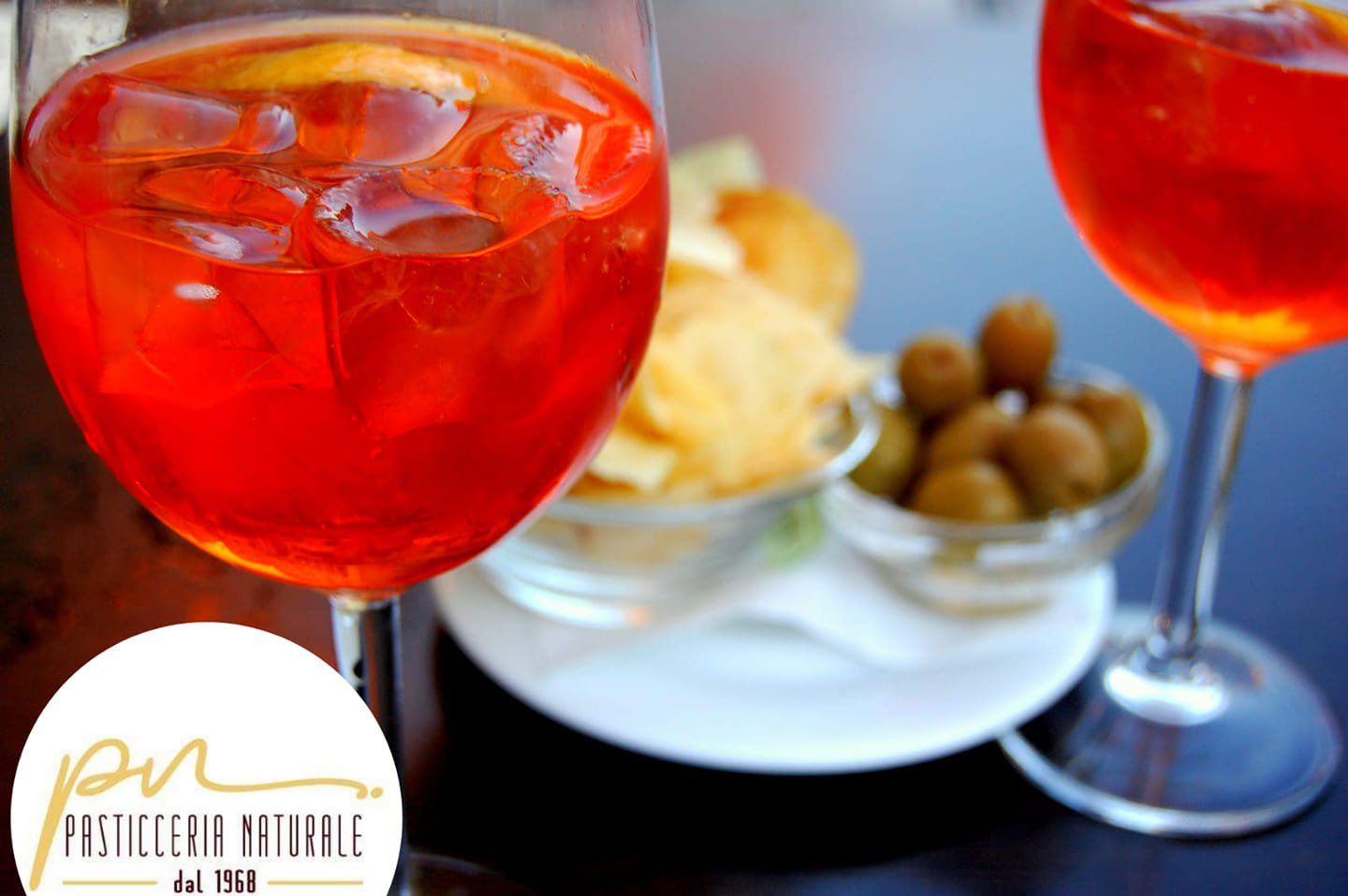 Due cocktail Aperol Spritz con stuzzichini, tra cui olive e patatine.