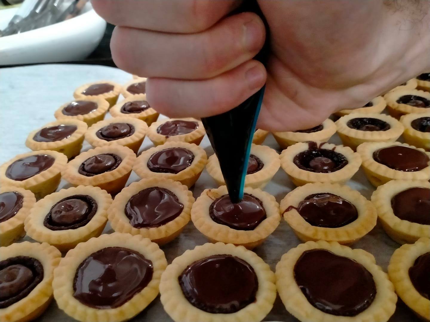 Distribuire a mano il ripieno di cioccolato nei gusci delle mini crostatine su un vassoio.