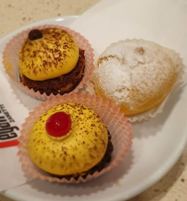 Tre piccoli pasticcini su un piatto bianco. Due hanno una glassa gialla, uno con una ciliegia. L'altro è glassato.