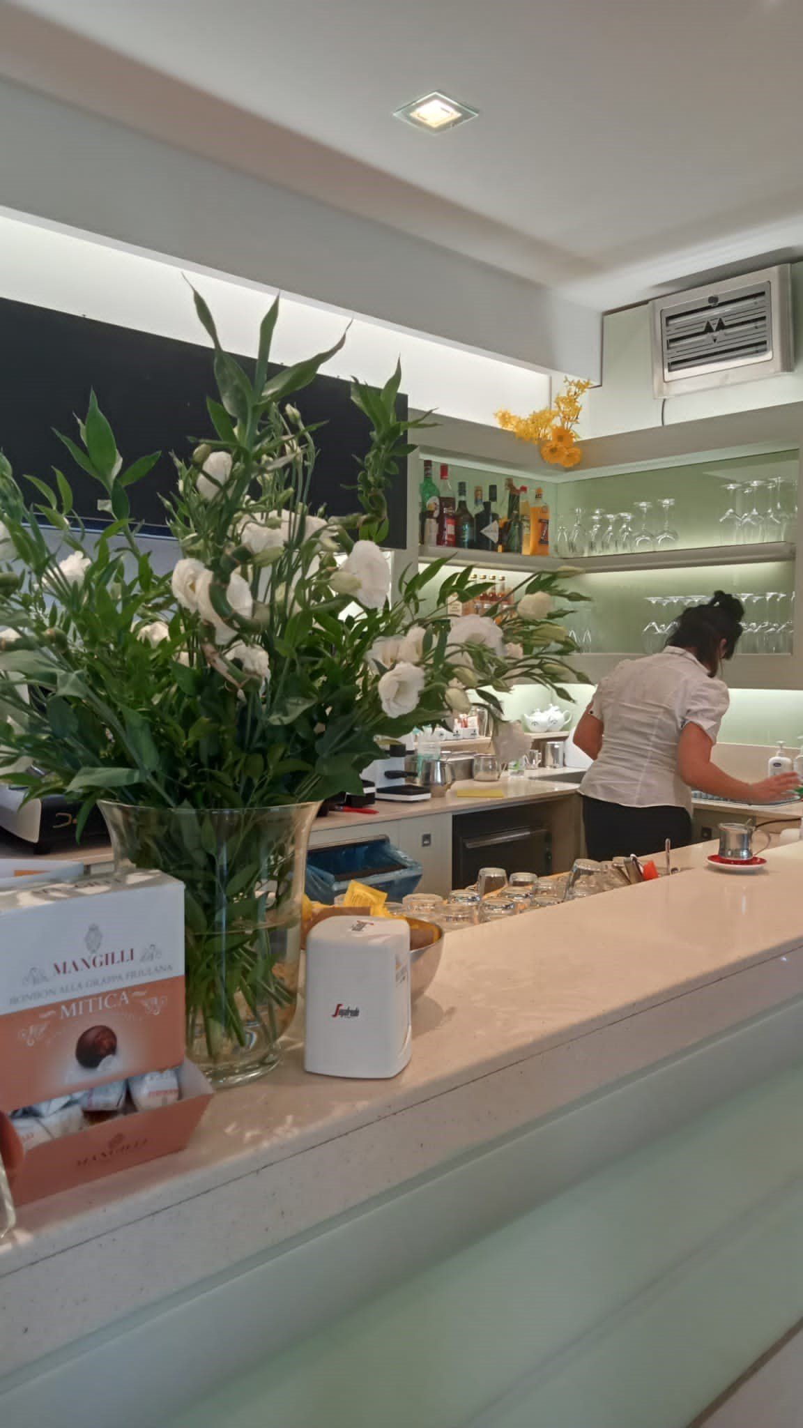 Interno del bar con barista, fiori e una vetrina di cioccolatini.