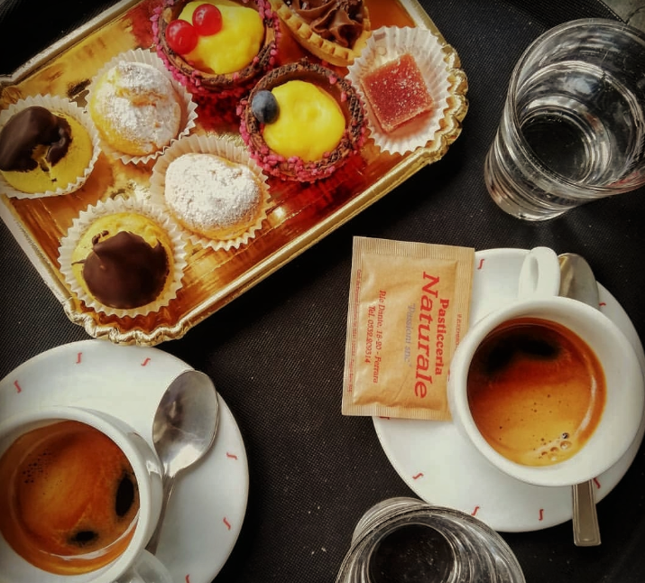 Vassoio di pasticcini, caffè espresso, bustina di zucchero e bicchieri d'acqua.