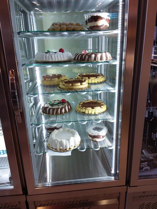 Torte esposte in una vetrina refrigerata con glassa e decorazioni bianche, marroni e gialle.