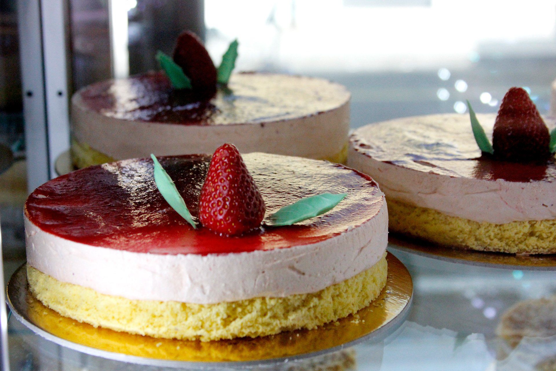 Tre torte alle fragole in una vetrina, con la parte superiore glassata e guarnizione di fragole su ciascuna.
