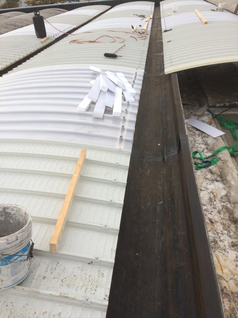 Vista dall'alto di pannelli di copertura ondulati in fase di installazione lungo uno stretto canale scuro sul tetto di un edificio.