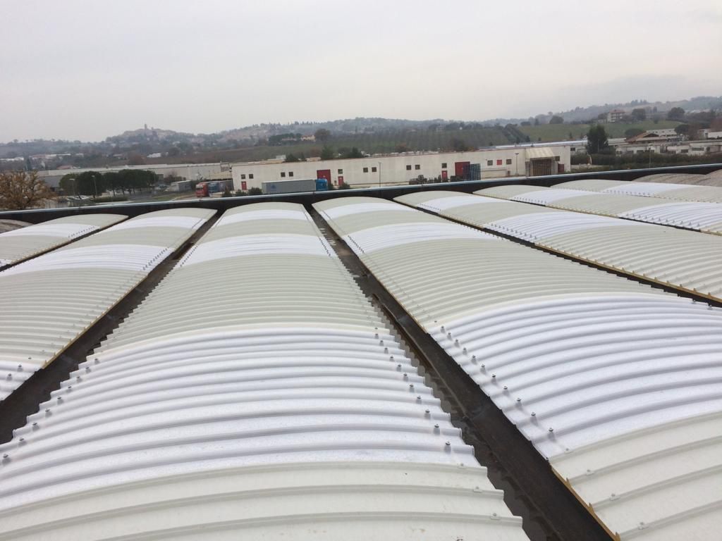 Una vista attraverso pannelli di copertura a volta a botte, ondulati e paralleli, di colore bianco, di un edificio industriale.