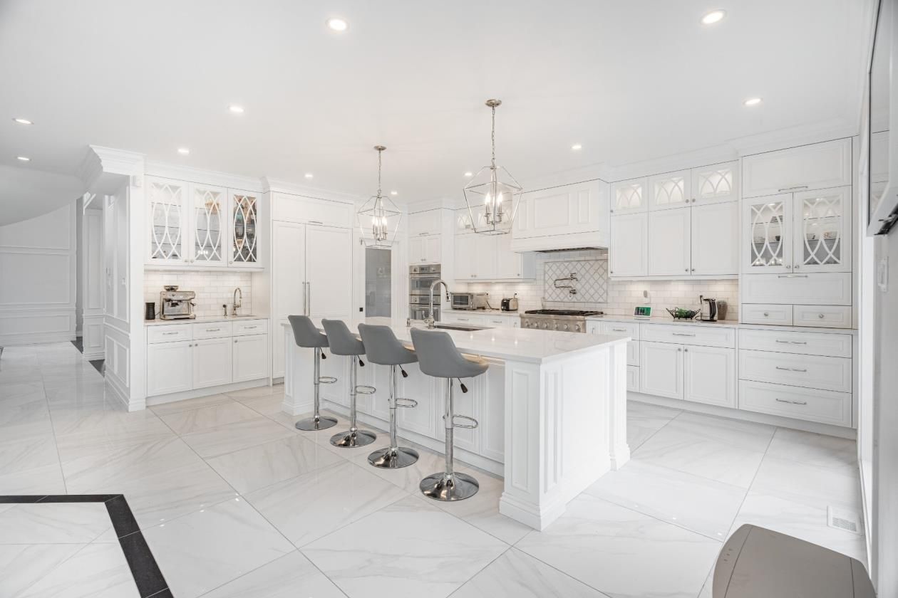 Une cuisine avec armoires et tabourets blancs et un grand îlot.