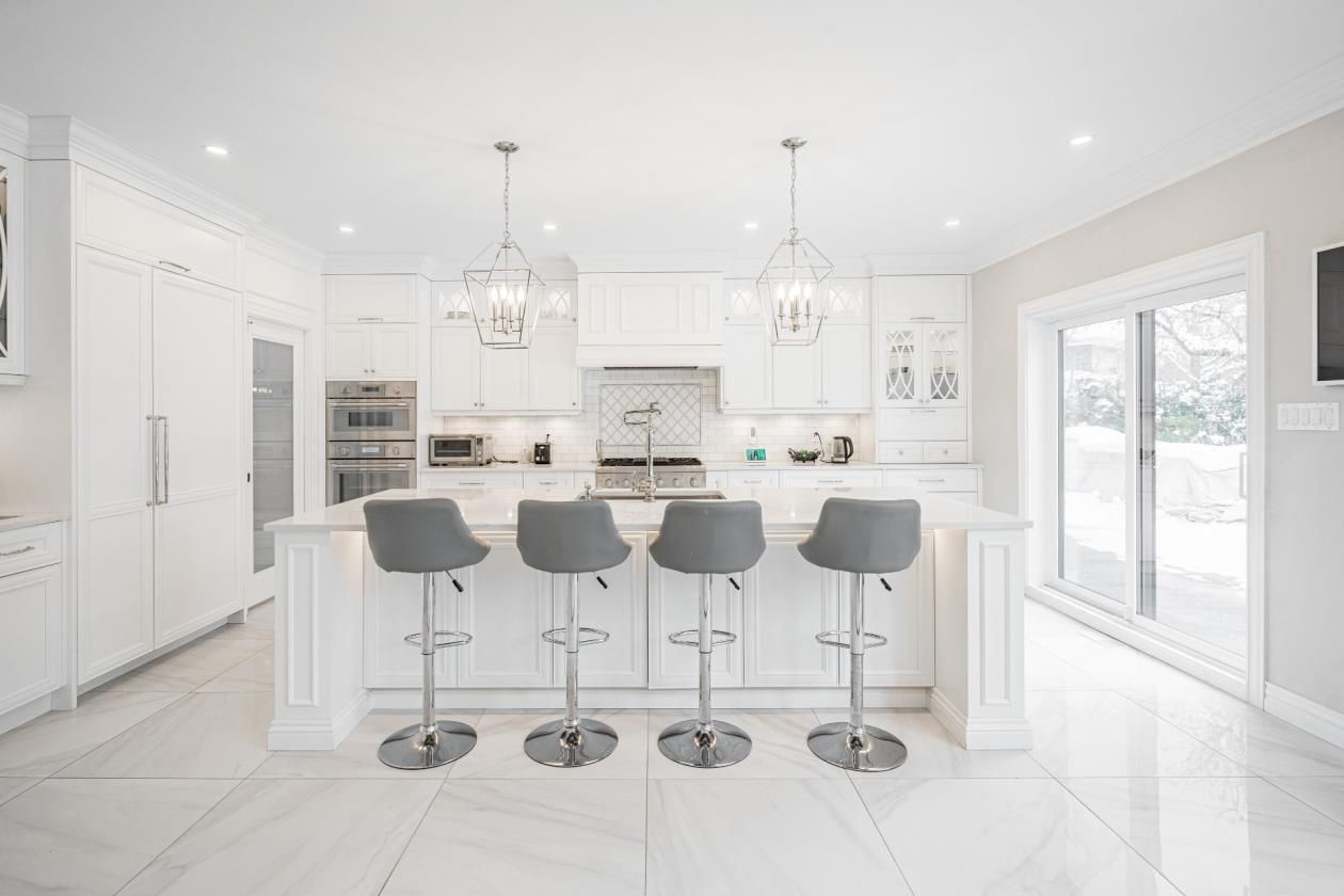 Une cuisine avec armoires et tabourets blancs et un grand îlot.