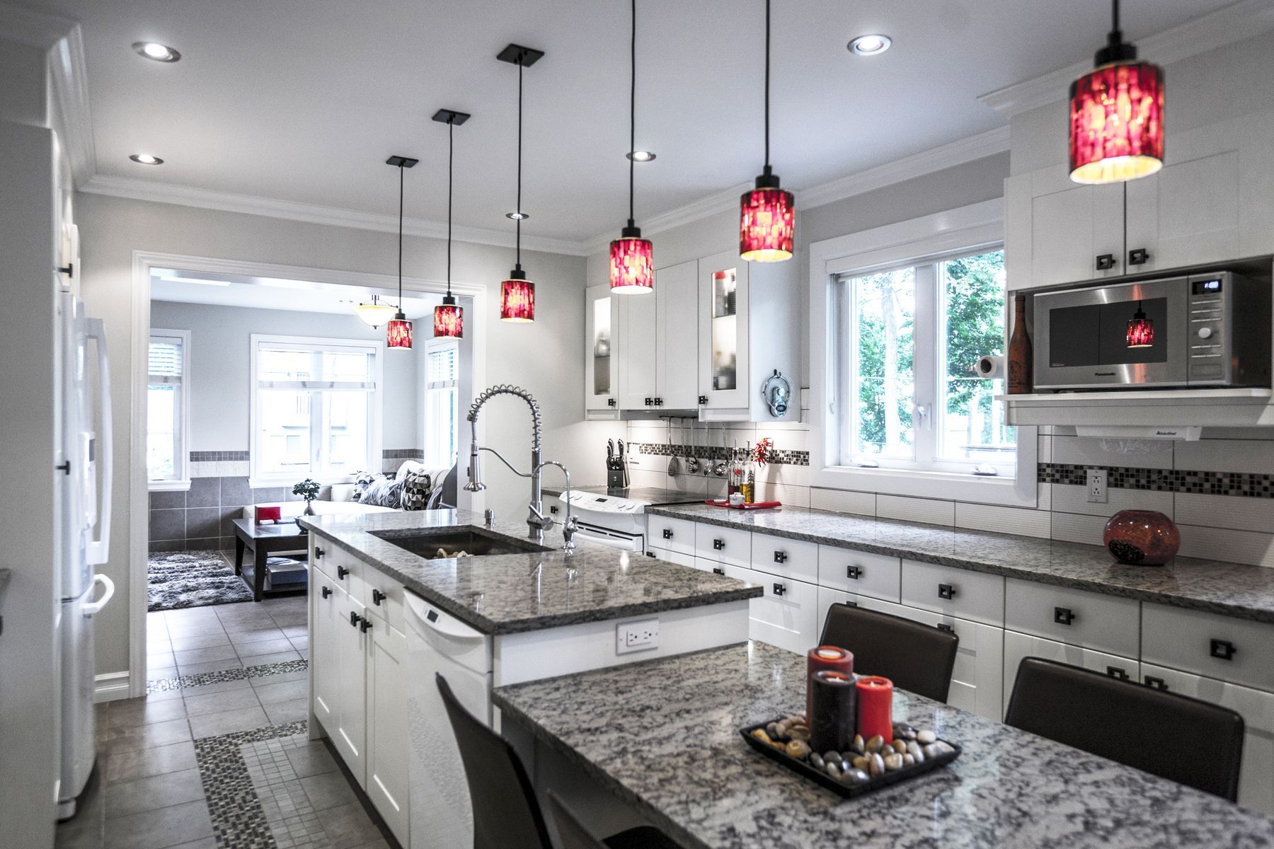 Une cuisine avec des armoires blanches, des comptoirs en granit et des suspensions rouges.