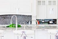 Une cuisine avec armoires blanches, comptoirs en granite, un évier et un robinet.