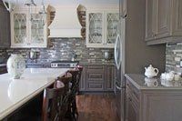 Une cuisine avec armoires grises, comptoirs blancs, électroménagers en acier inoxydable et un grand îlot.