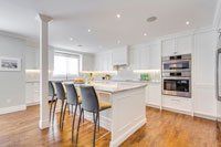 Une cuisine avec armoires blanches, électroménagers en acier inoxydable, planchers de bois franc et un grand îlot.