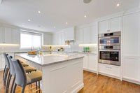 Une cuisine avec armoires blanches et électroménagers en acier inoxydable et un grand îlot.