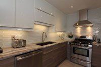 Une cuisine avec électroménagers en acier inoxydable, armoires blanches, comptoirs en granit, un évier et une cuisinière.