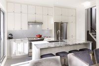 Une cuisine avec armoires blanches, comptoirs en granit, électroménagers en acier inoxydable et un grand îlot.