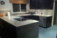 Une cuisine avec des armoires noires, des appareils électroménagers en acier inoxydable, un évier et une fenêtre.