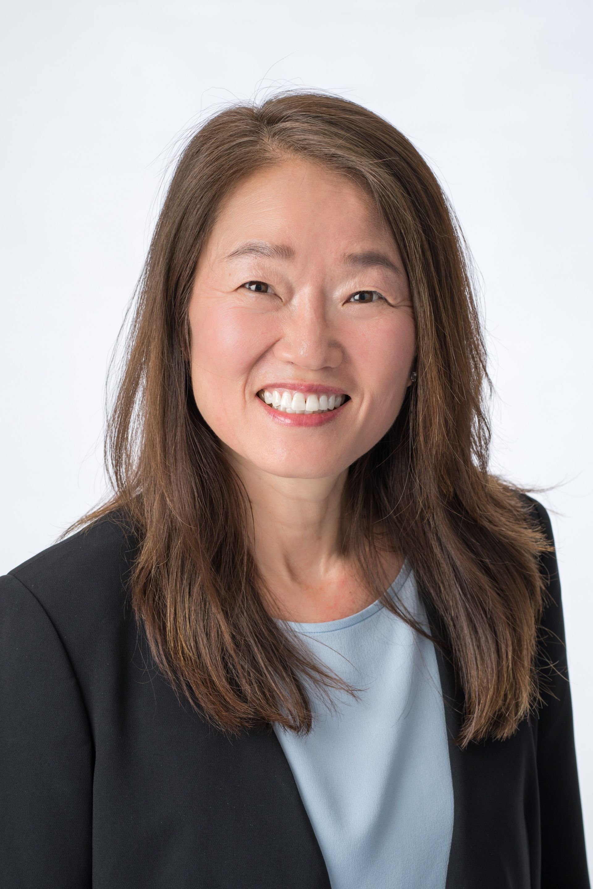 Woman with brown hair smiles, wearing a black blazer and light blue shirt.