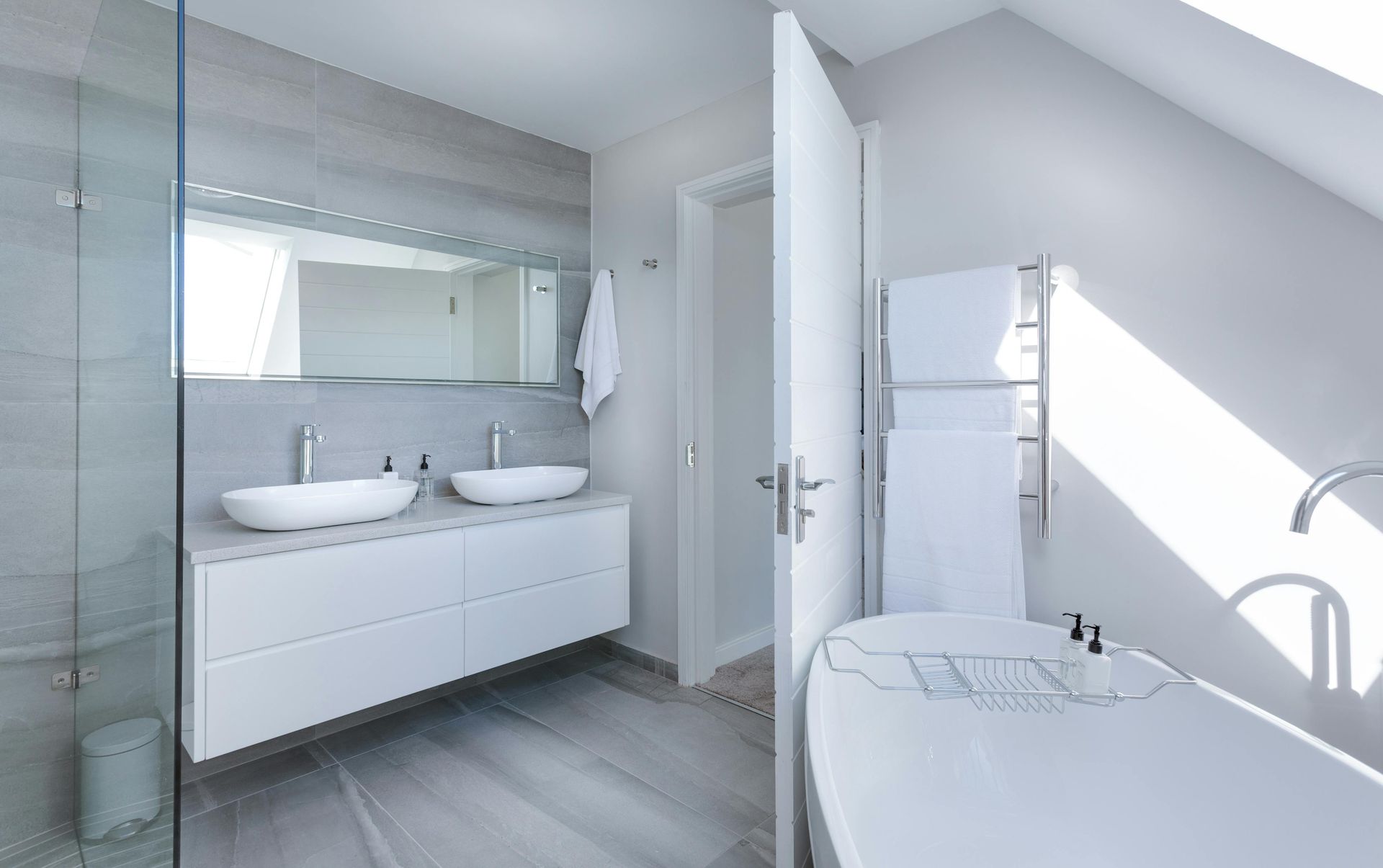 Modern white bathroom with double sinks, glass shower, and freestanding bathtub.