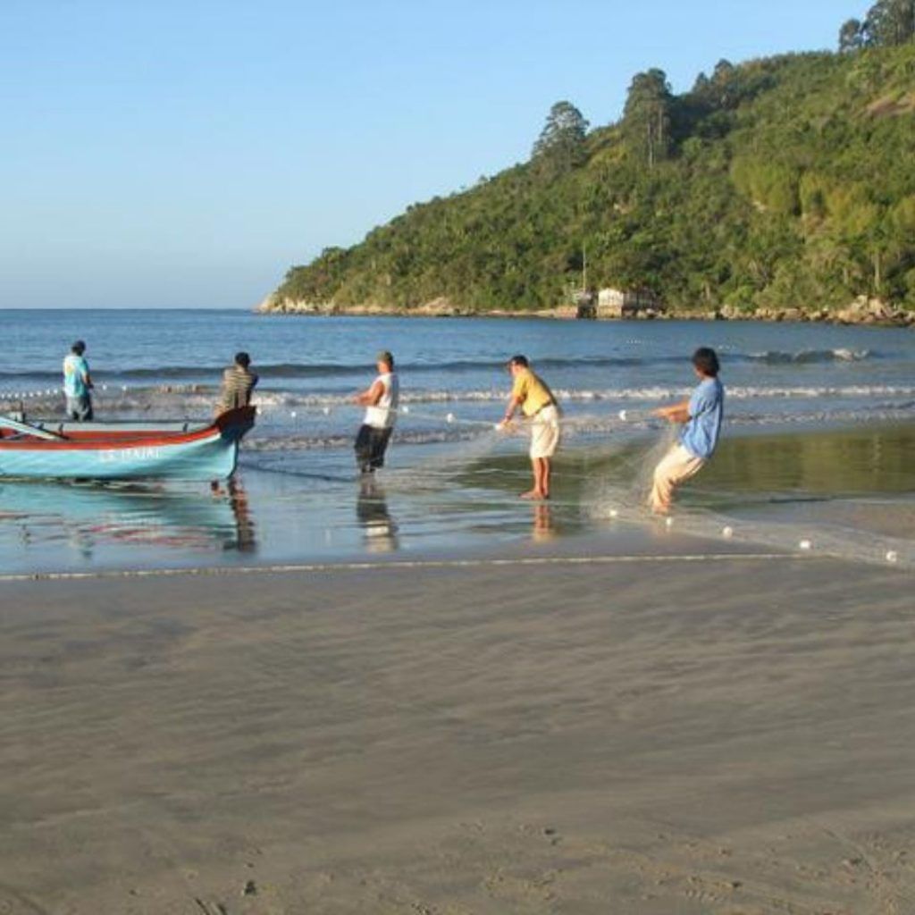 Um grupo de pessoas pescando em uma praia com barcos ao fundo