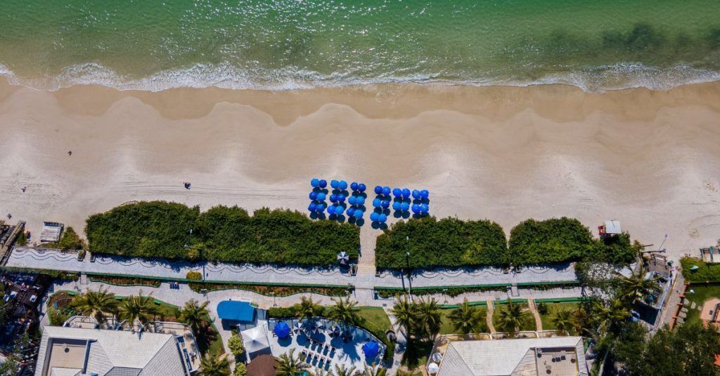 Uma vista aérea de uma praia com guarda-sóis azuis e uma piscina.