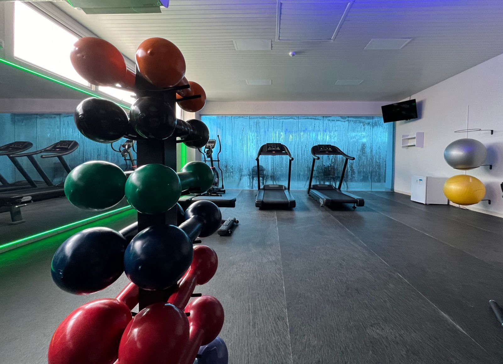 Uma academia com muitos aparelhos de ginástica e uma piscina ao fundo.