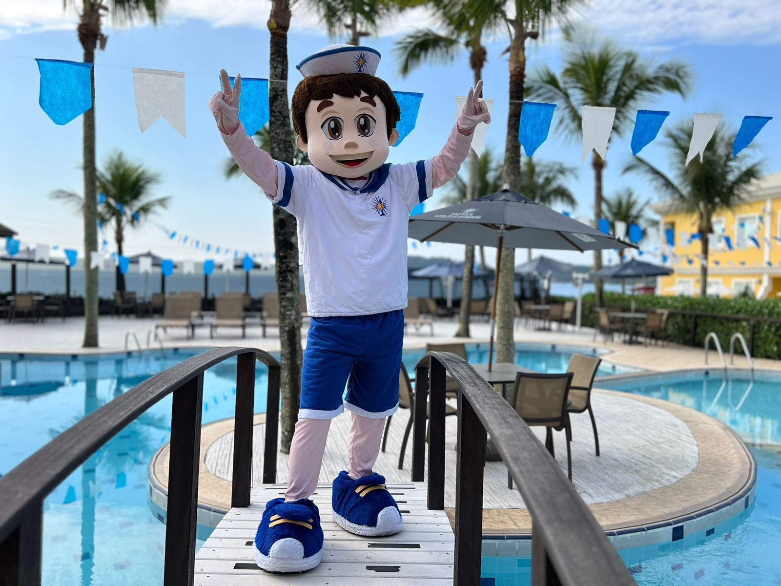 Um mascote está em uma ponte de madeira sobre uma piscina.